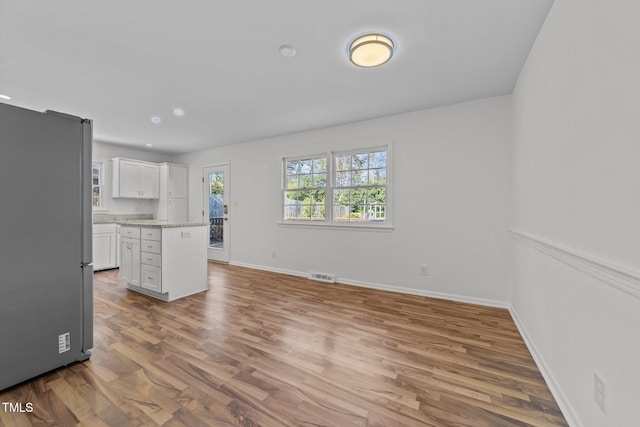 kitchen featuring a center island, stainless steel fridge, light stone countertops, light hardwood / wood-style floors, and white cabinetry