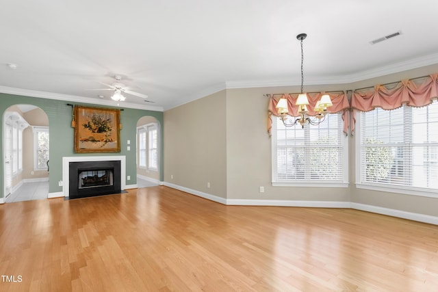 unfurnished living room featuring wood-type flooring, ceiling fan with notable chandelier, plenty of natural light, and crown molding