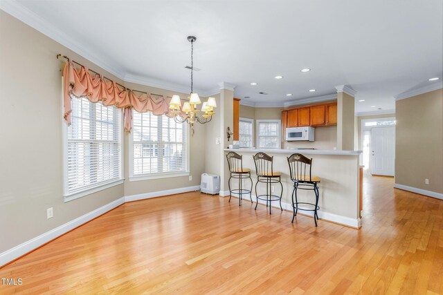 kitchen with pendant lighting, crown molding, light hardwood / wood-style flooring, kitchen peninsula, and a chandelier