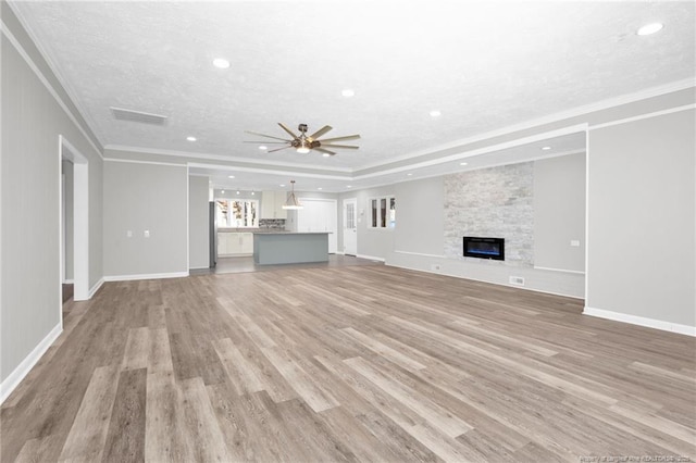 unfurnished living room with ornamental molding, a textured ceiling, ceiling fan, a fireplace, and light hardwood / wood-style floors