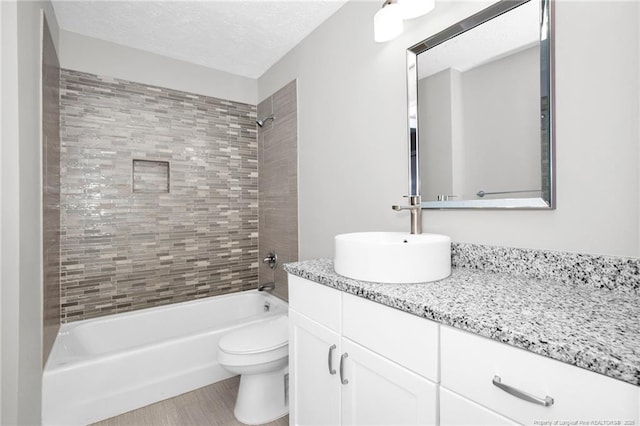 full bathroom featuring vanity, tiled shower / bath combo, a textured ceiling, and toilet