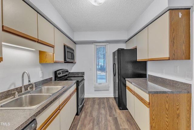 kitchen featuring black appliances, dark countertops, a sink, and light wood-style floors