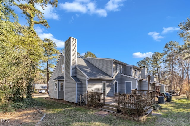 view of property exterior featuring roof with shingles, a chimney, a lawn, cooling unit, and a wooden deck