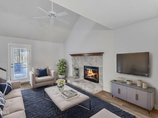 living area with ceiling fan, light wood-style flooring, a fireplace, and vaulted ceiling