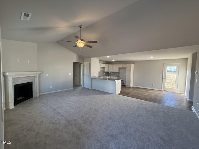 unfurnished living room with dark colored carpet, ceiling fan, sink, and vaulted ceiling