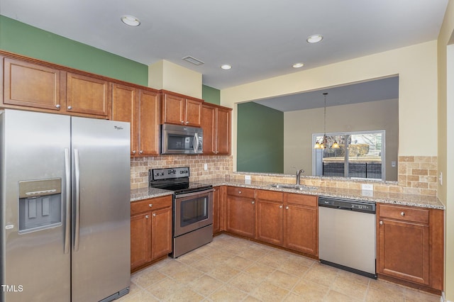 kitchen with sink, stainless steel appliances, light stone counters, decorative light fixtures, and a chandelier