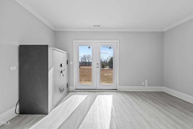 empty room featuring crown molding, french doors, and light wood-type flooring