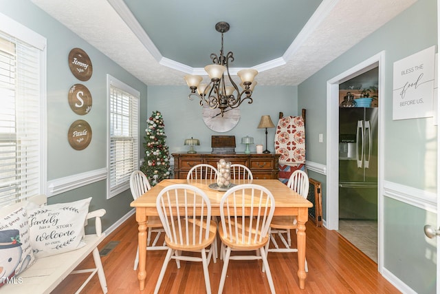 dining space featuring a raised ceiling, crown molding, hardwood / wood-style flooring, a textured ceiling, and a chandelier