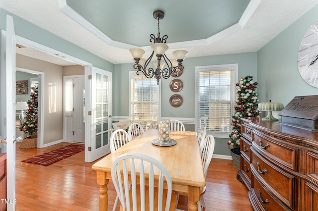 dining area with a tray ceiling, a chandelier, ornamental molding, and hardwood / wood-style flooring