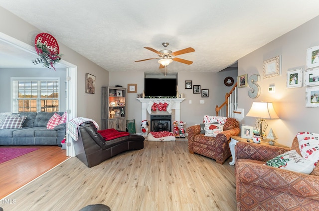 living room featuring a tile fireplace, a textured ceiling, light wood-type flooring, and ceiling fan