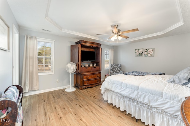 bedroom featuring a tray ceiling, ceiling fan, crown molding, and light wood-type flooring