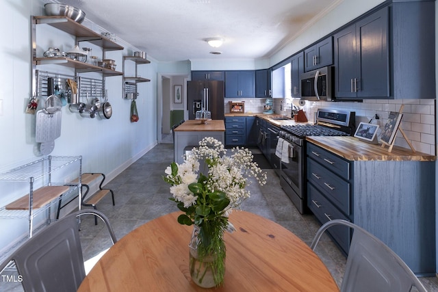 kitchen with wooden counters, blue cabinets, sink, tasteful backsplash, and stainless steel appliances