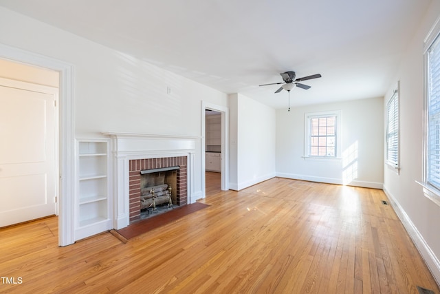 unfurnished living room with light wood-type flooring, ceiling fan, built in features, and a fireplace