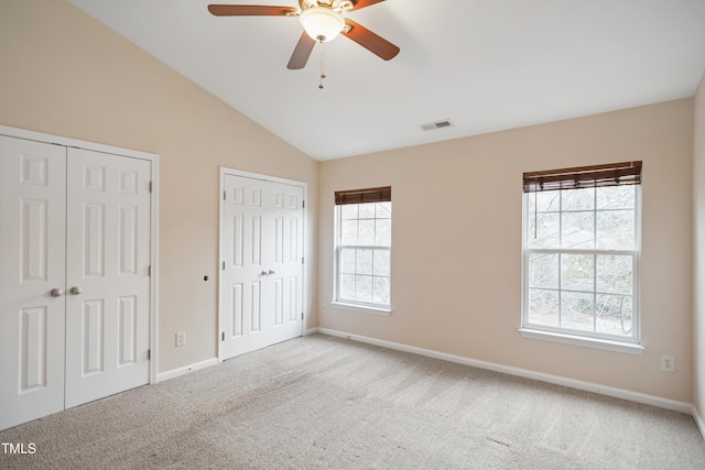 unfurnished bedroom with multiple closets, ceiling fan, light colored carpet, and vaulted ceiling