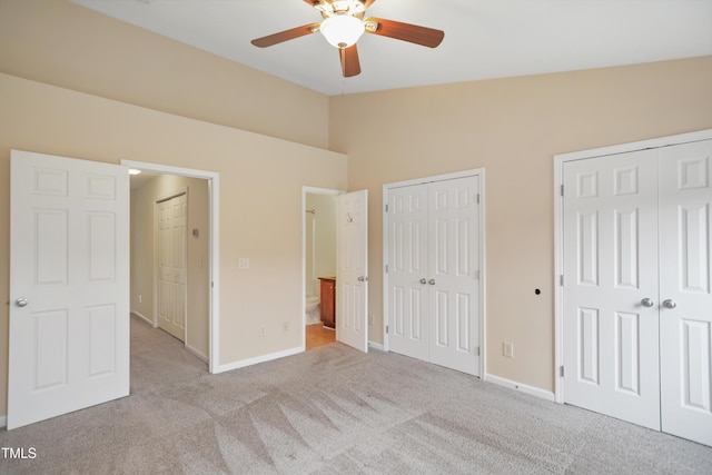 unfurnished bedroom with ceiling fan, vaulted ceiling, light carpet, and multiple closets