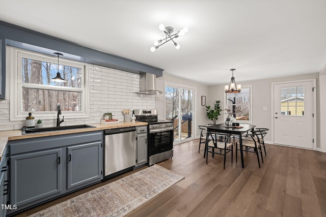 kitchen featuring stainless steel appliances, wall chimney range hood, sink, decorative light fixtures, and an inviting chandelier