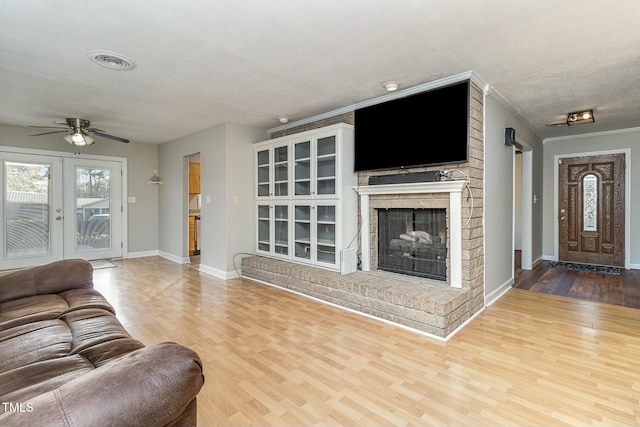 living room featuring ceiling fan, french doors, a brick fireplace, crown molding, and hardwood / wood-style floors