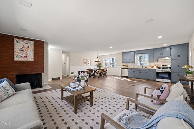 living room featuring sink, wood-type flooring, a brick fireplace, and an inviting chandelier