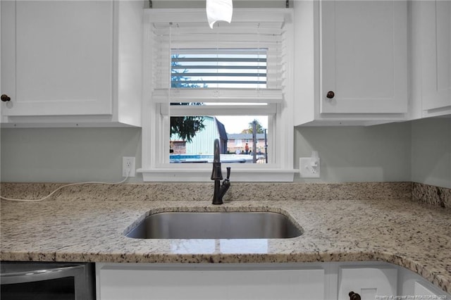 kitchen featuring wine cooler, light stone counters, white cabinetry, and sink