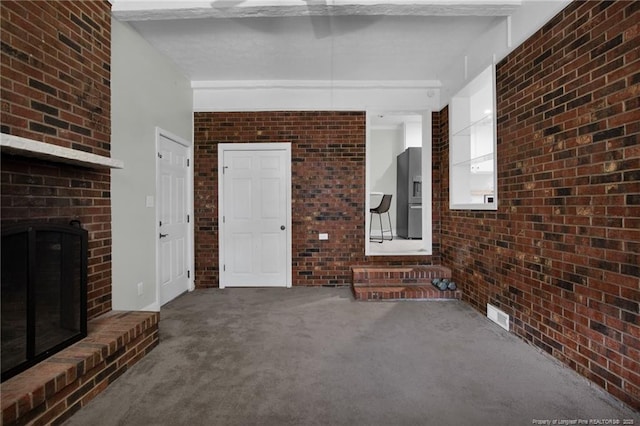 unfurnished living room featuring carpet flooring, brick wall, and a brick fireplace