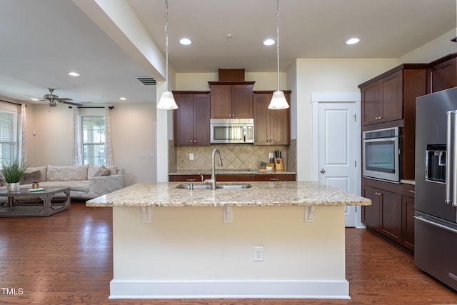 kitchen with pendant lighting, a breakfast bar area, a kitchen island with sink, light stone counters, and stainless steel appliances