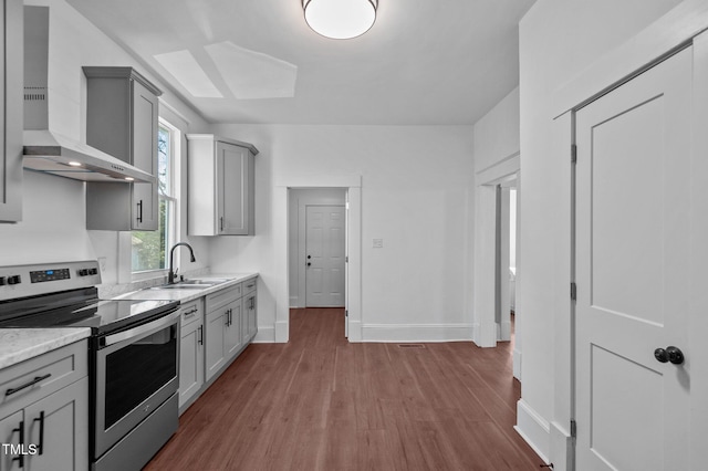 kitchen featuring stainless steel electric range, sink, wall chimney exhaust hood, gray cabinets, and wood-type flooring