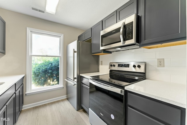 kitchen featuring decorative backsplash, appliances with stainless steel finishes, light wood-type flooring, and light stone countertops