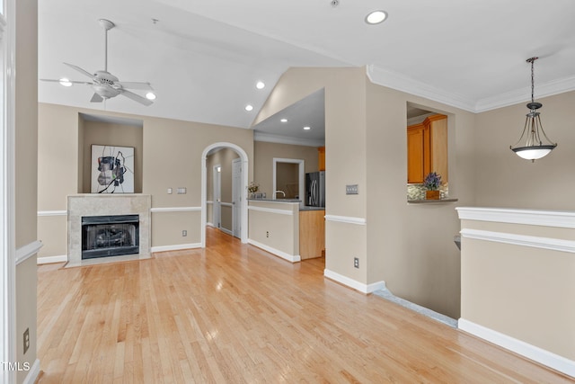 unfurnished living room featuring a tile fireplace, ceiling fan, crown molding, light hardwood / wood-style floors, and lofted ceiling