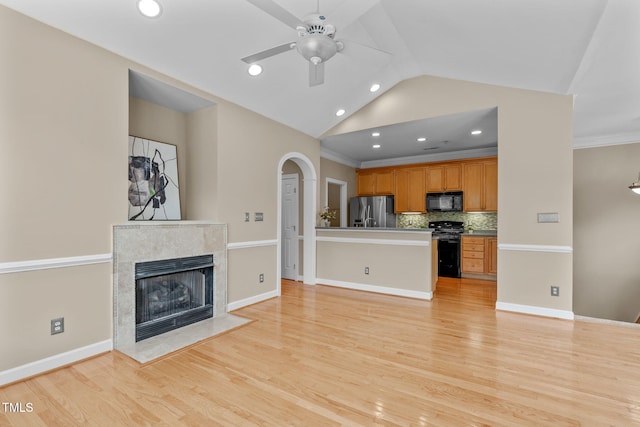 unfurnished living room featuring ceiling fan, light hardwood / wood-style flooring, vaulted ceiling, a fireplace, and ornamental molding