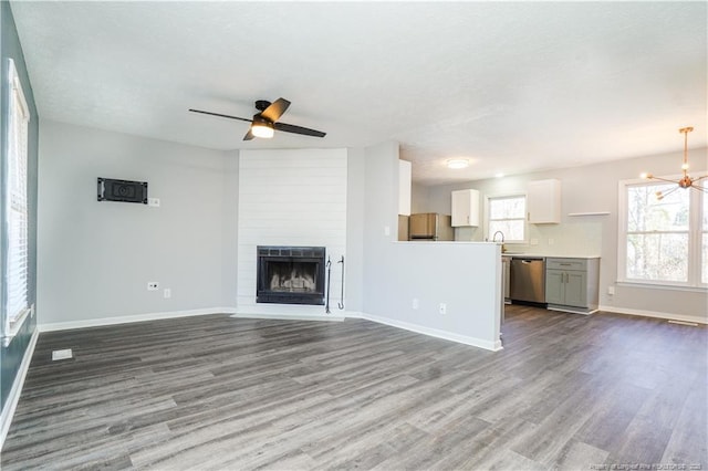 unfurnished living room with a large fireplace, ceiling fan with notable chandelier, and light wood-type flooring