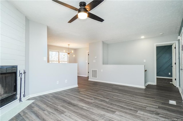 unfurnished living room with ceiling fan with notable chandelier, a large fireplace, dark hardwood / wood-style flooring, and a textured ceiling