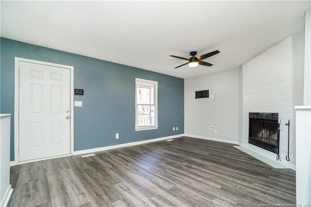 unfurnished living room with ceiling fan, a large fireplace, and dark wood-type flooring