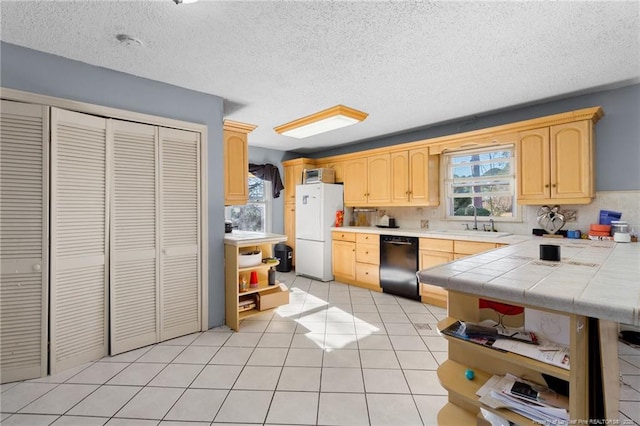 kitchen with tile countertops, white refrigerator, light tile patterned floors, black dishwasher, and light brown cabinetry