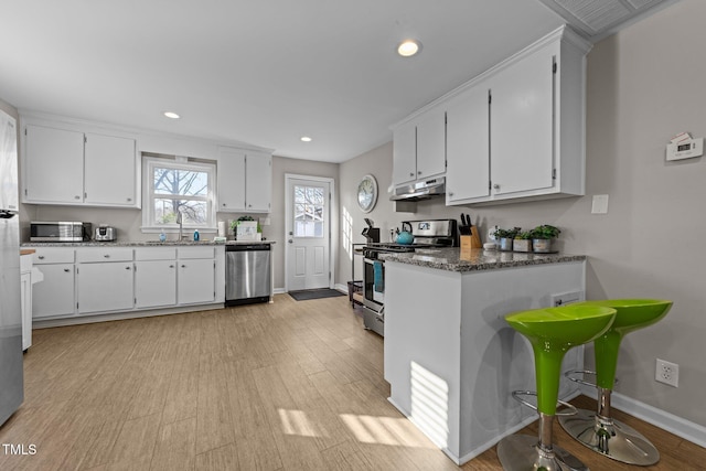 kitchen with white cabinets, stainless steel appliances, dark stone countertops, sink, and light wood-type flooring