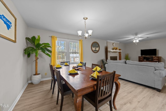 dining space featuring ceiling fan with notable chandelier, light hardwood / wood-style flooring, and a fireplace