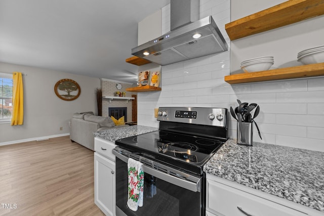 kitchen with wall chimney exhaust hood, white cabinets, stainless steel range with electric stovetop, light stone countertops, and decorative backsplash