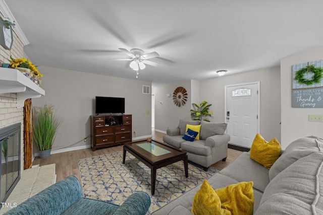 living room featuring a fireplace, light wood-type flooring, and ceiling fan