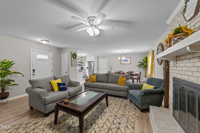 living room featuring a fireplace, ceiling fan with notable chandelier, and light wood-type flooring