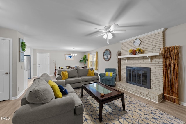 living room featuring ceiling fan with notable chandelier, a brick fireplace, and light hardwood / wood-style flooring