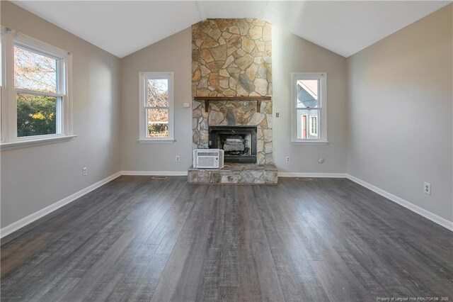 unfurnished living room featuring an AC wall unit, dark hardwood / wood-style floors, a stone fireplace, and lofted ceiling