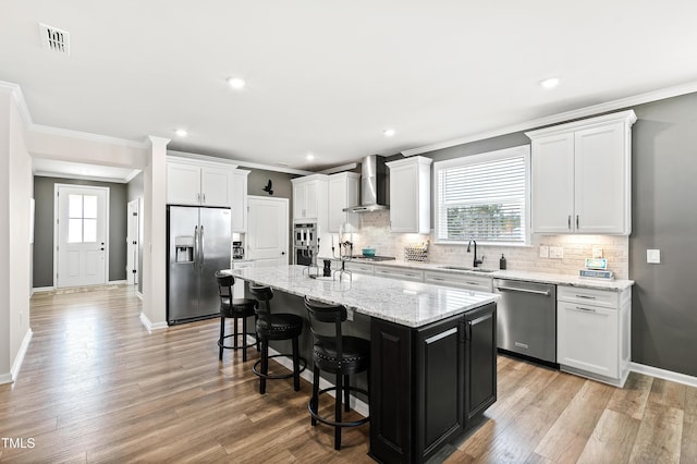 kitchen featuring a kitchen island, appliances with stainless steel finishes, white cabinetry, a kitchen breakfast bar, and wall chimney range hood