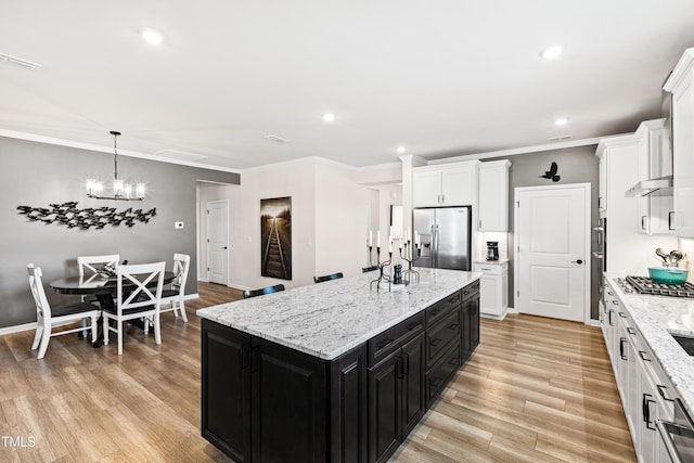 kitchen featuring appliances with stainless steel finishes, pendant lighting, white cabinets, a kitchen island with sink, and light hardwood / wood-style floors