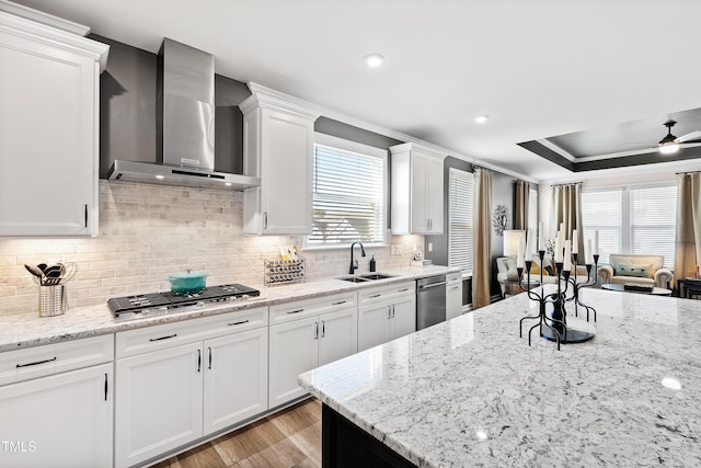 kitchen featuring sink, white cabinetry, light stone counters, stainless steel appliances, and wall chimney range hood