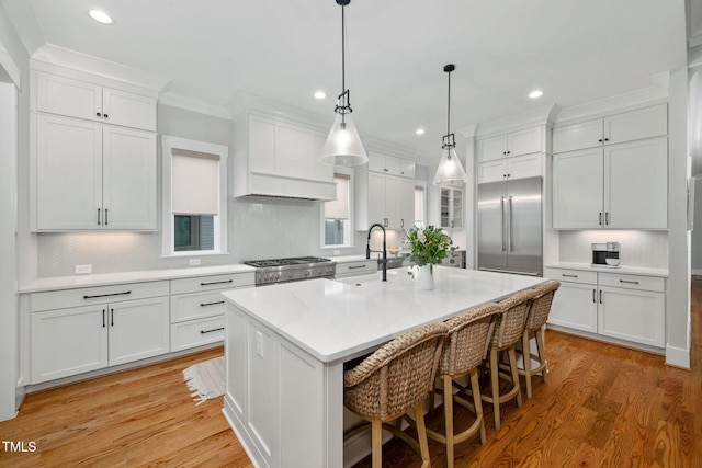 kitchen with white cabinets, a kitchen island with sink, built in fridge, and stove