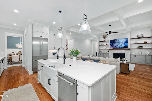 kitchen featuring appliances with stainless steel finishes, white cabinetry, sink, hanging light fixtures, and a center island with sink