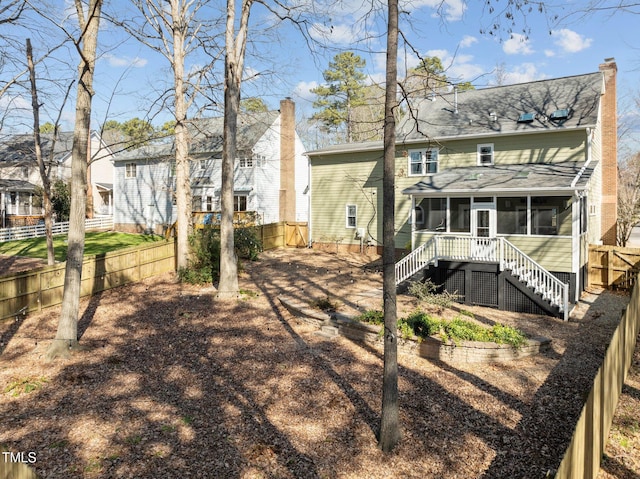 rear view of house featuring a sunroom, a fenced backyard, a chimney, and stairs