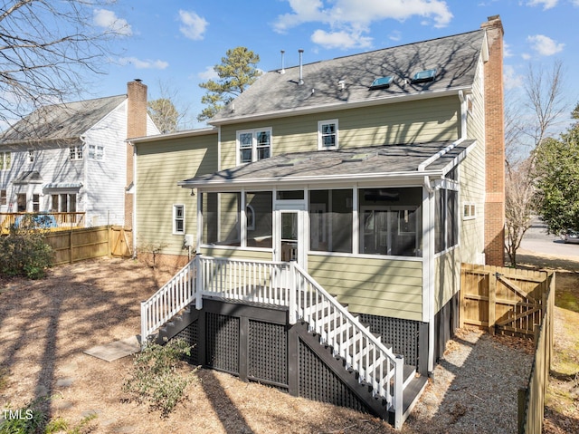 back of house featuring a chimney, a sunroom, a fenced backyard, and stairway