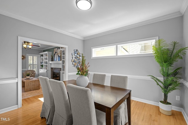 dining space featuring ornamental molding, a glass covered fireplace, light wood-style flooring, and baseboards