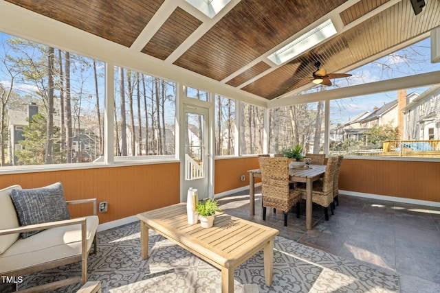 sunroom featuring a ceiling fan, vaulted ceiling with skylight, wood ceiling, and plenty of natural light