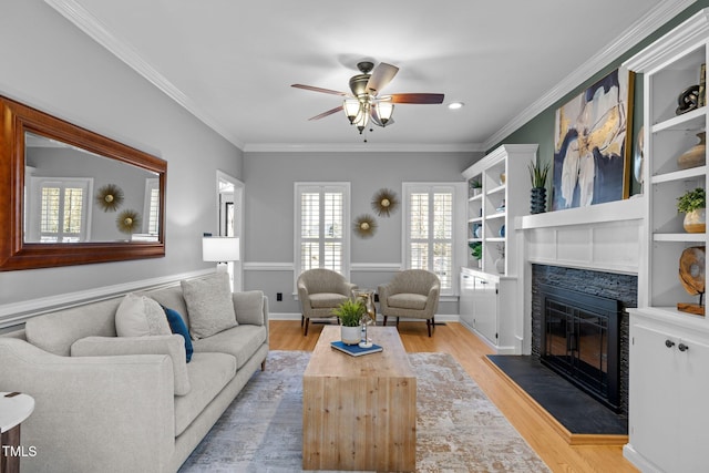 living room featuring crown molding, light wood-style floors, a glass covered fireplace, ceiling fan, and baseboards